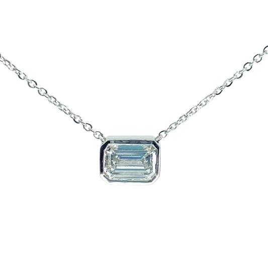 White gold necklace with a bezel set emerald cut diamond shining from the center.